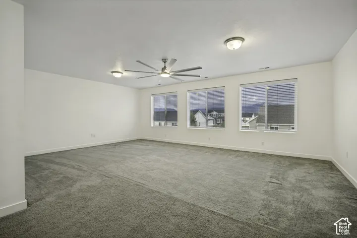 Spacious room featuring neutral carpeting, three large windows with blinds, and two ceiling-mounted light fixtures, one with an integrated fan