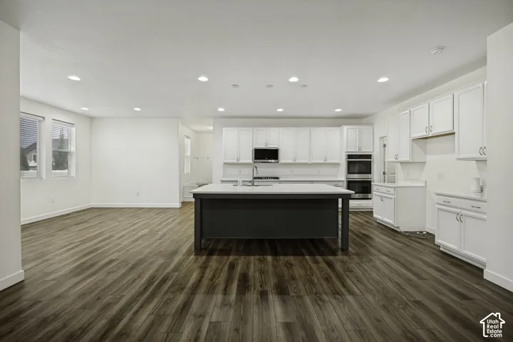 Expansive living space featuring wood-finish flooring, recessed lighting, and a kitchen with white cabinetry