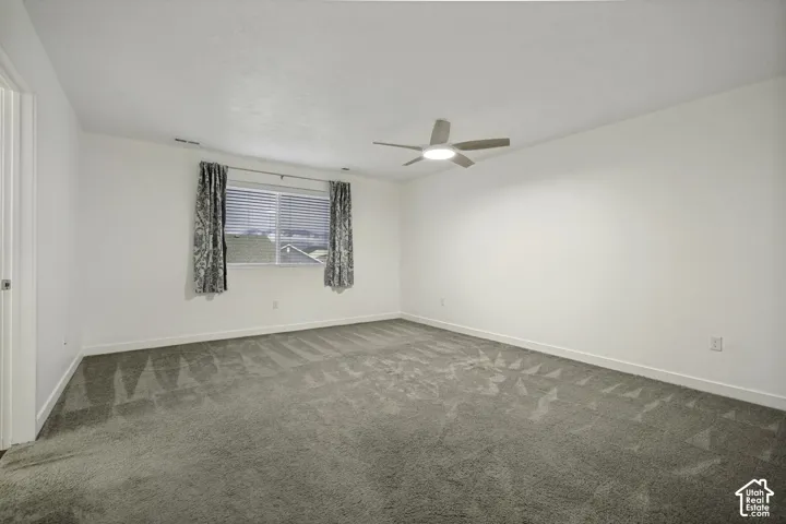 Spacious room featuring neutral carpeting, a modern ceiling fan with integrated lighting, and a large window with blinds