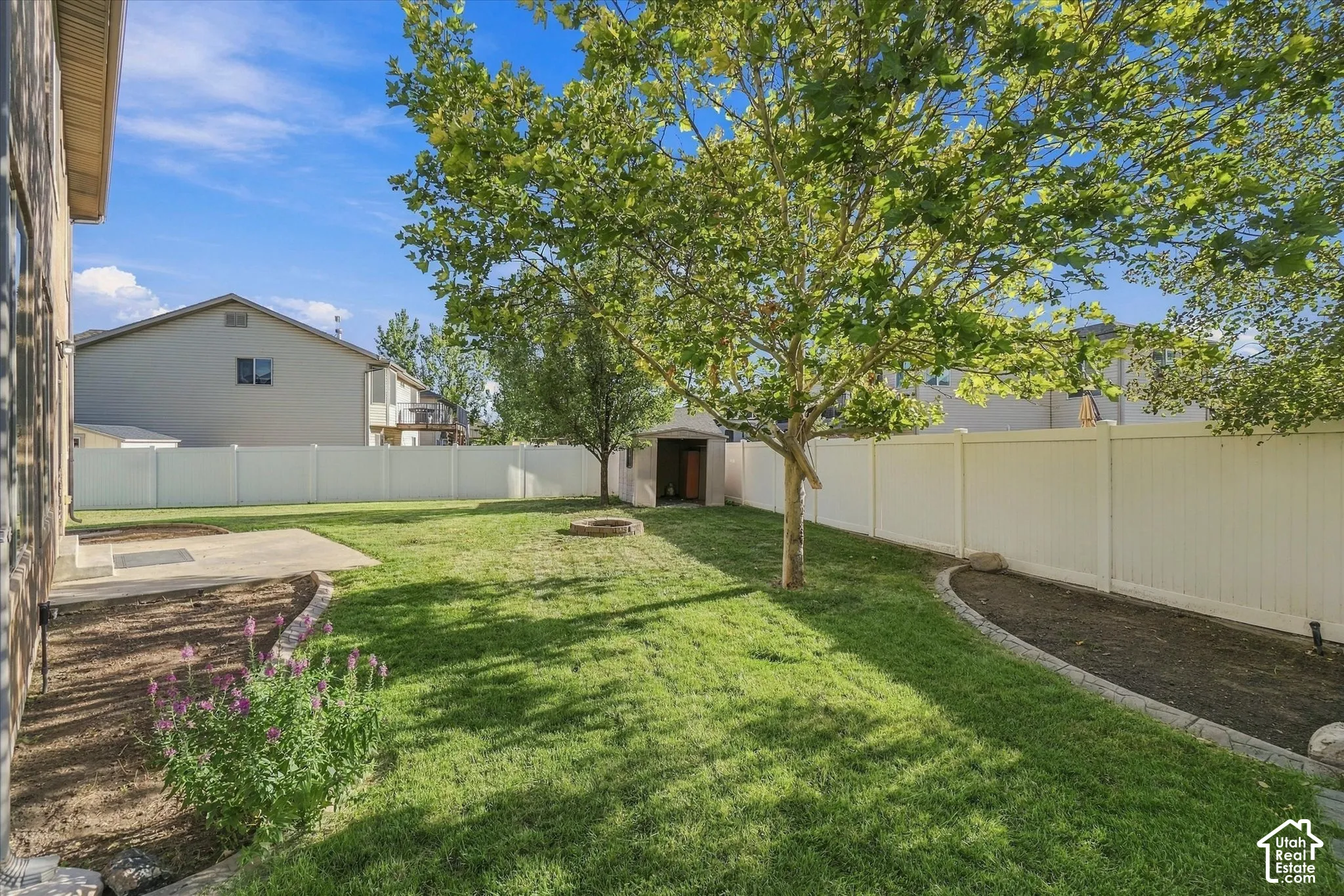 Expansive backyard featuring a manicured lawn, established trees, concrete patio, and a storage shed