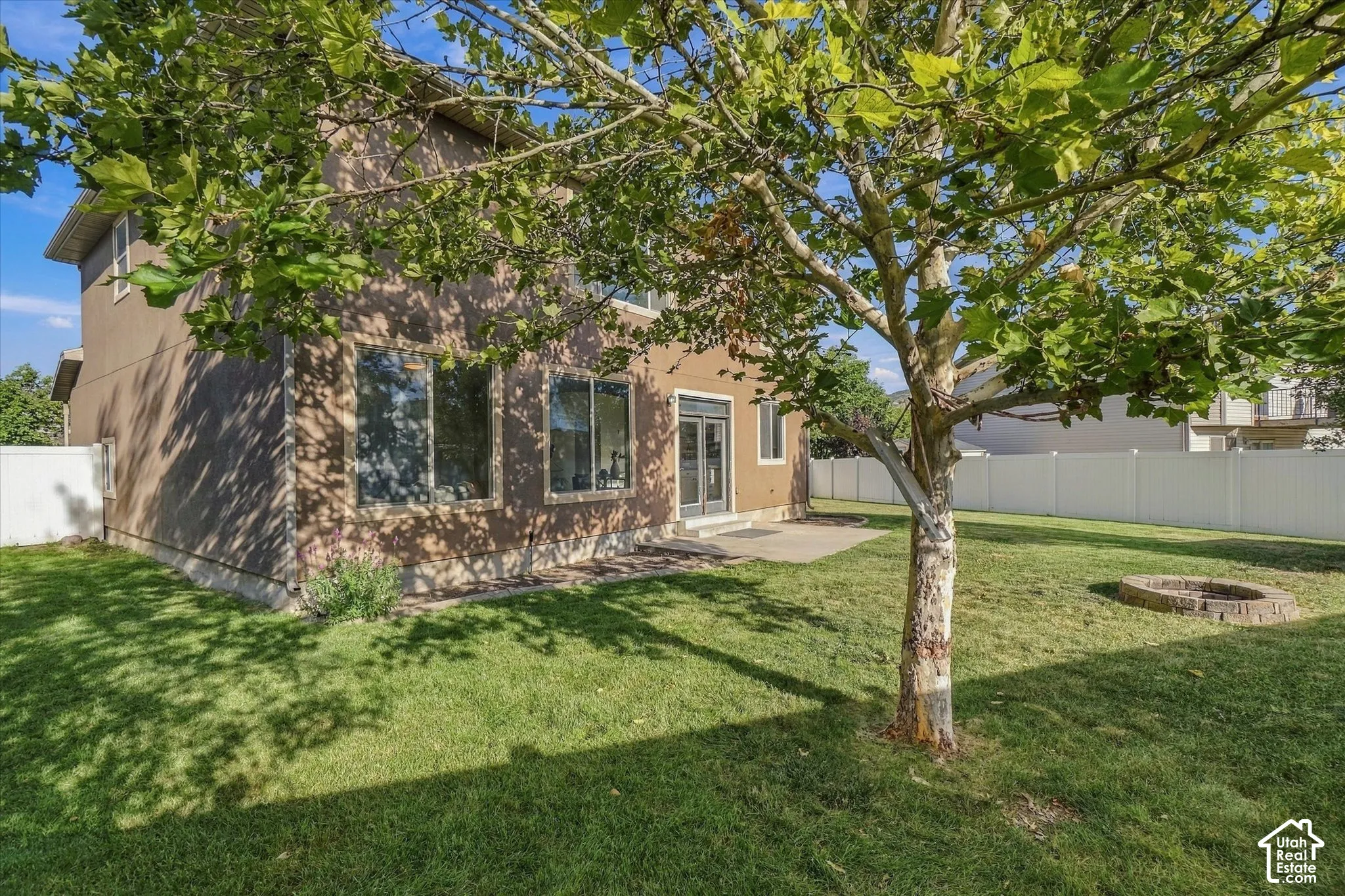 Private backyard with a mature tree, a stone fire pit, and a stucco exterior with multiple windows
