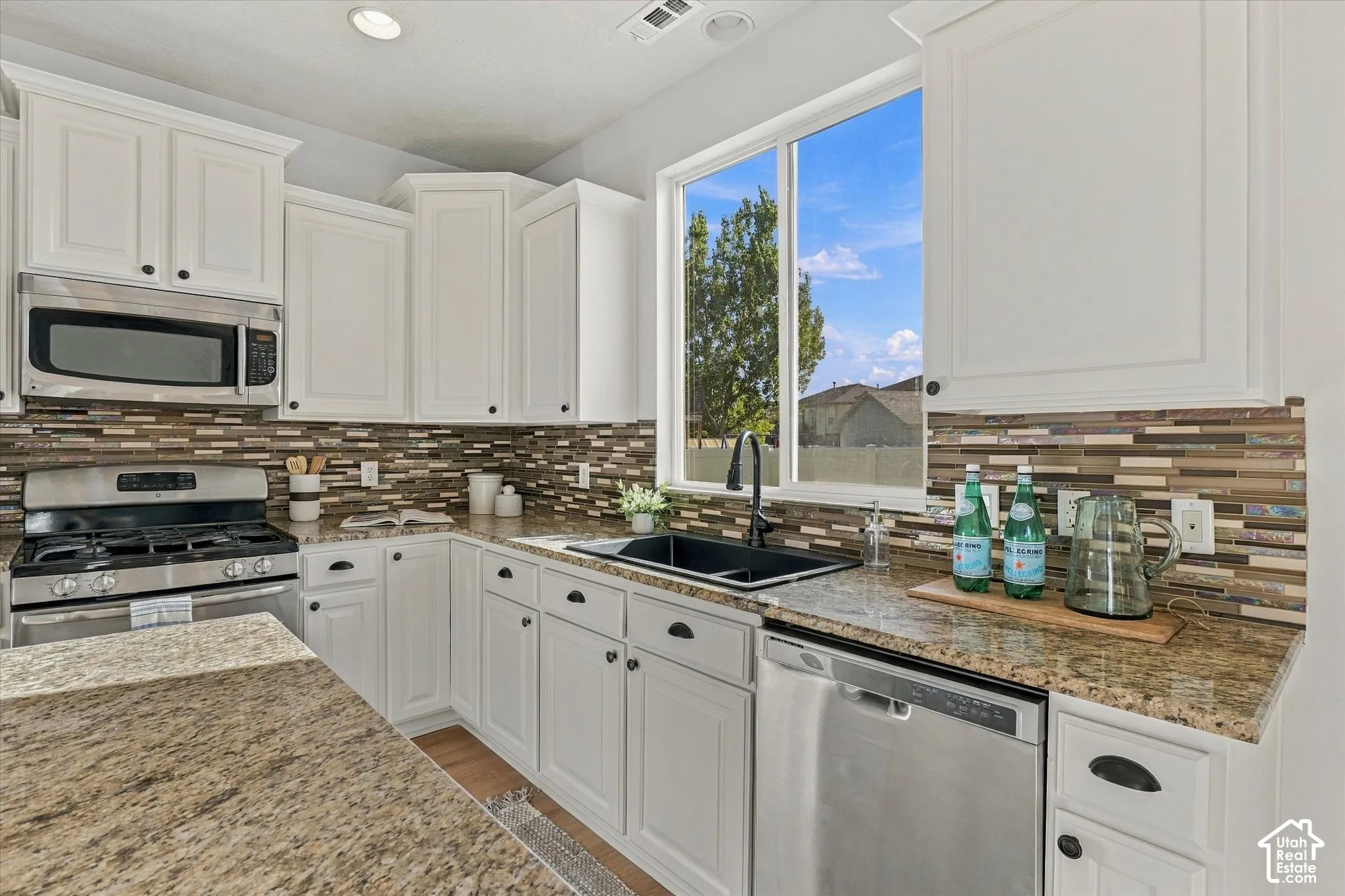 White cabinetry, stainless steel appliances, granite countertops, tile backsplash, and a black undermount sink with a black faucet