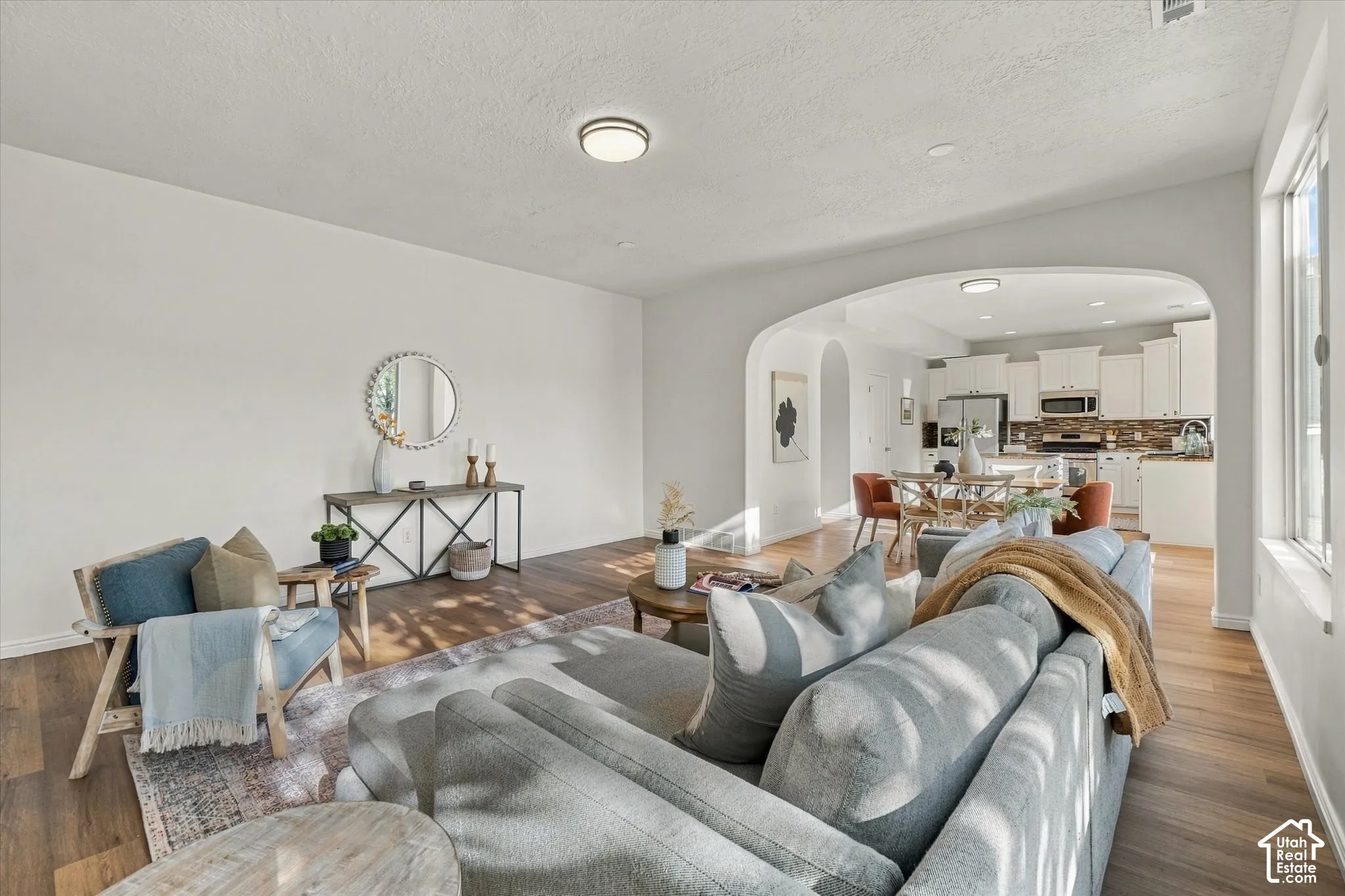 Open-concept design featuring wood-finish flooring, an arched doorway, and ample natural light from multiple windows