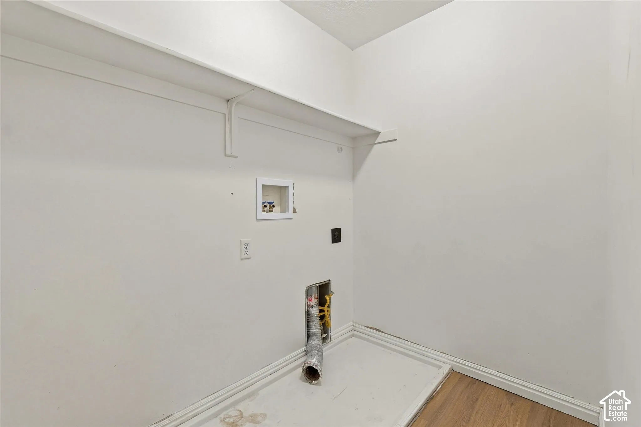 Laundry area featuring a wall-mounted shelf, utility hookups, and wood-finish flooring