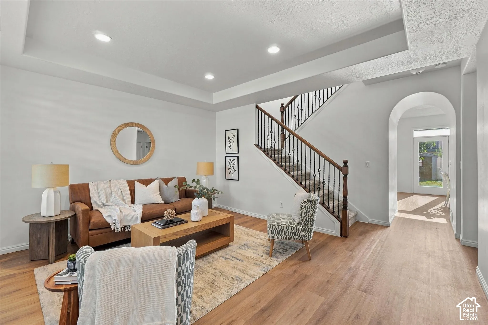 Recessed lighting, tray ceiling, wood-finish flooring, wrought iron stair balusters, and an arched entryway