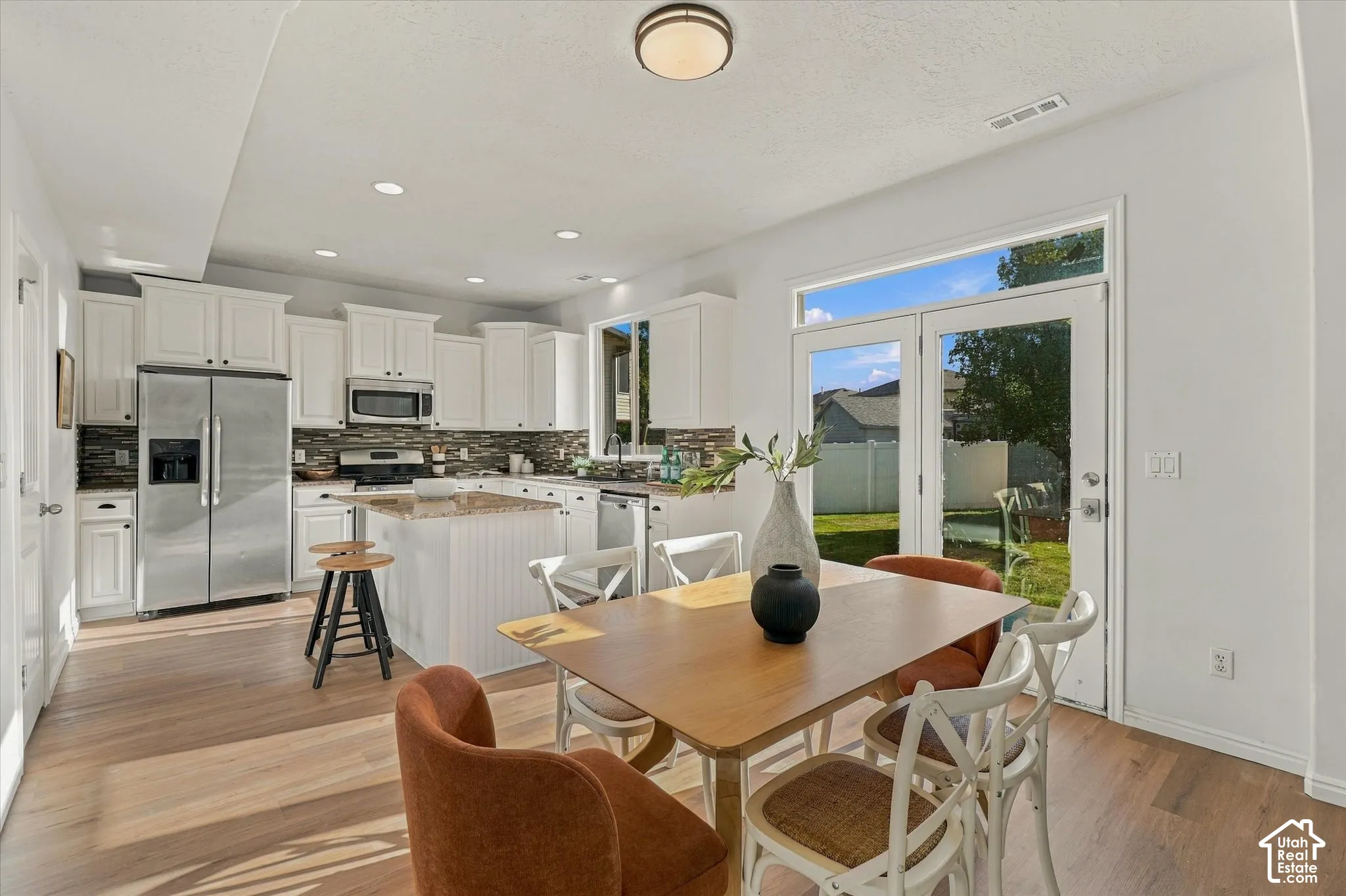 Kitchen featuring wood-finish flooring, white cabinetry, a central island with a beadboard base, stainless steel appliances, and a glass-paned door leading to the exterior