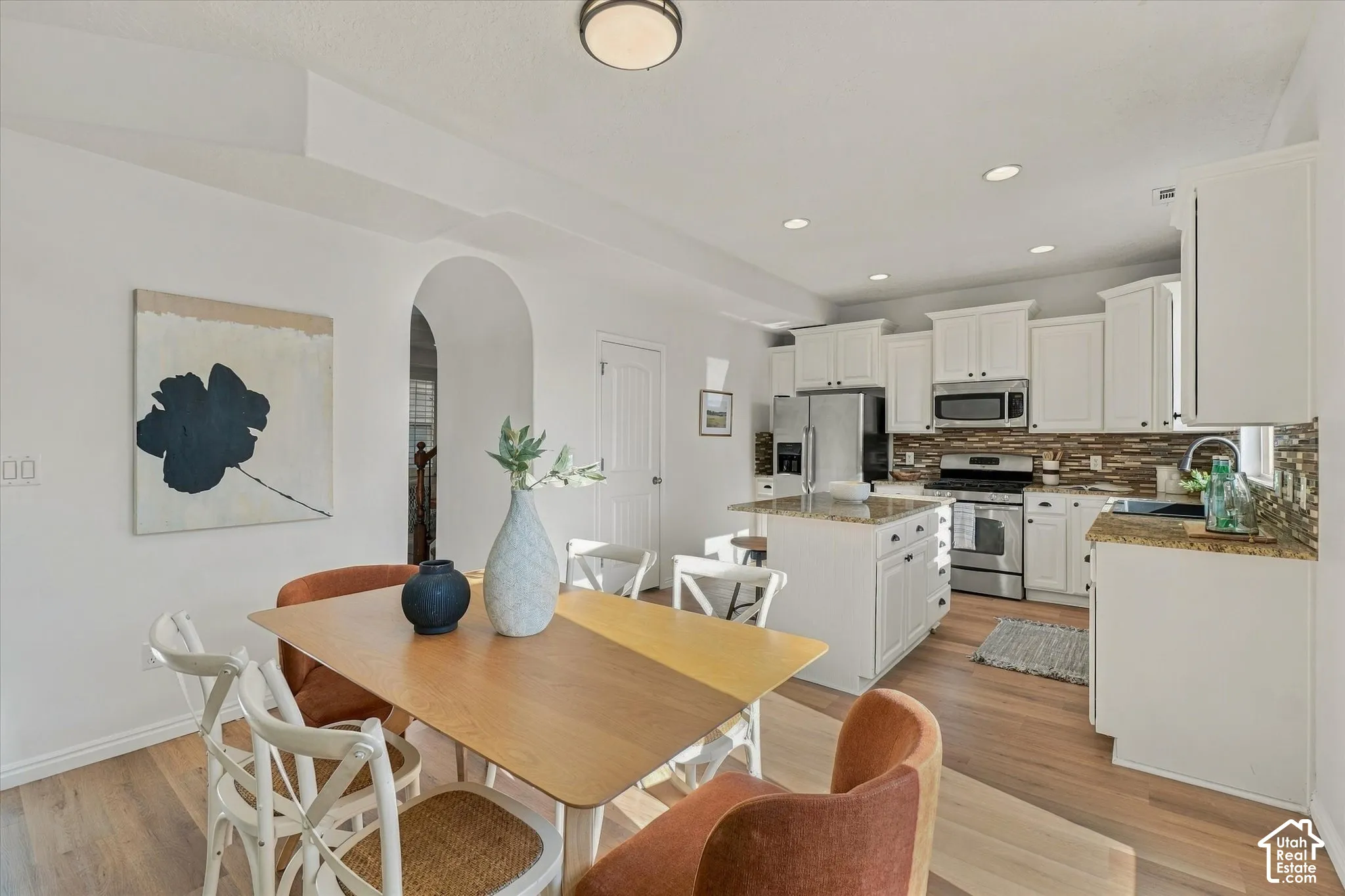 Kitchen featuring white cabinetry, stainless steel appliances, a center island with seating, granite countertops, and a tile backsplash