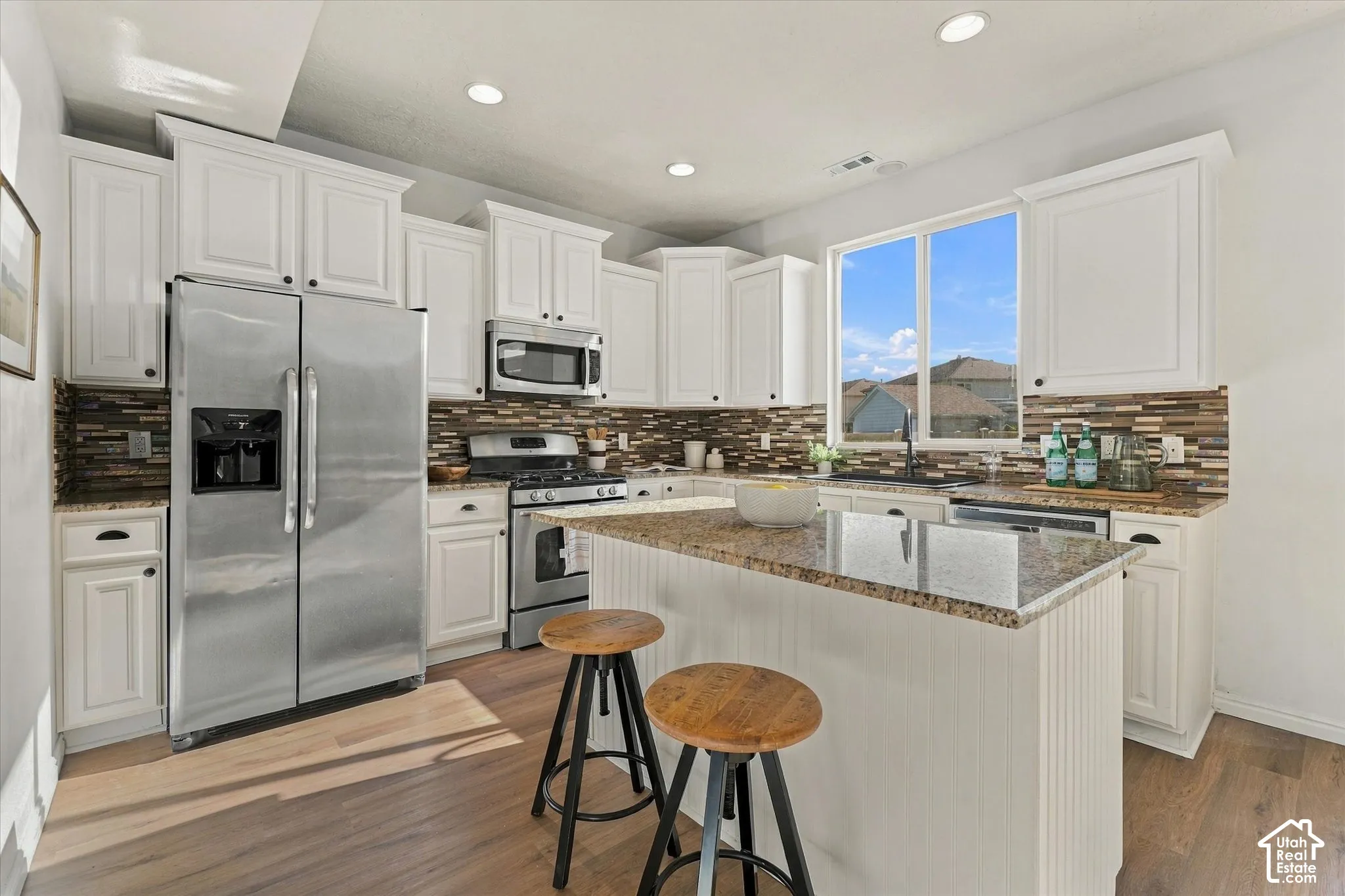 Kitchen featuring white cabinetry, stainless steel appliances, a multi-tone tile backsplash, and wood-finish flooring