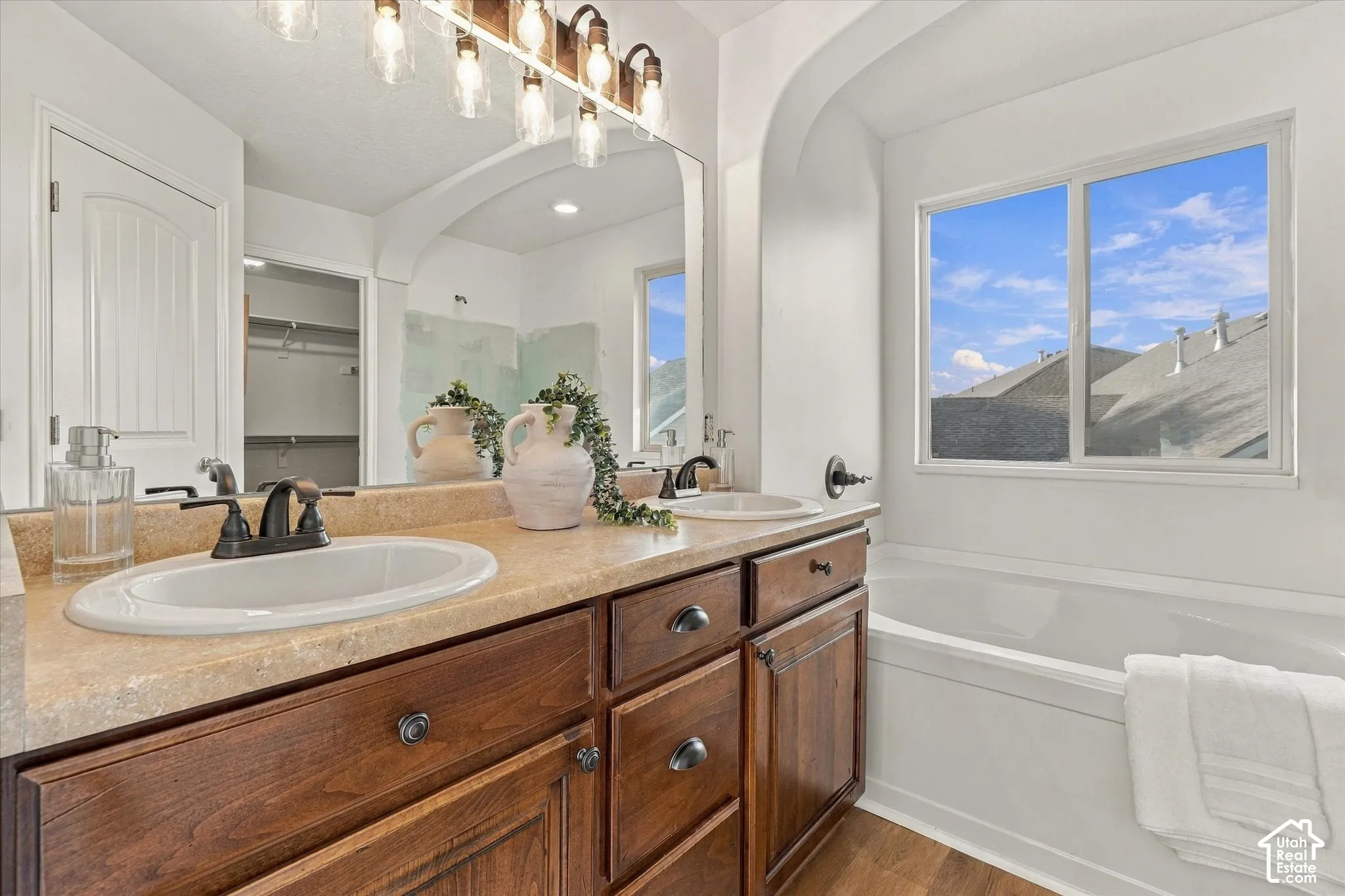 Dual sink vanity with dark wood-finish cabinetry, a large built-in mirror, and an integrated soaking tub