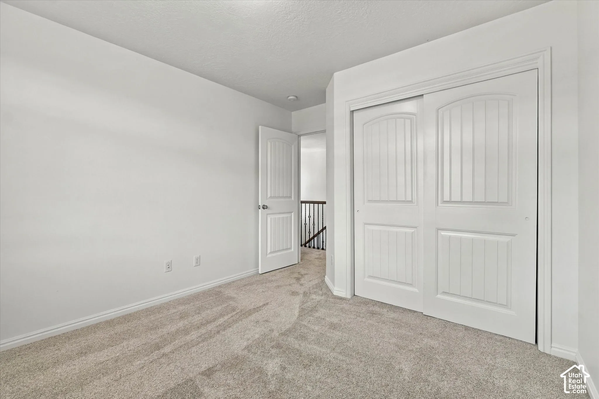 Neutral tone carpeting, white walls, white trim, and white sliding closet doors