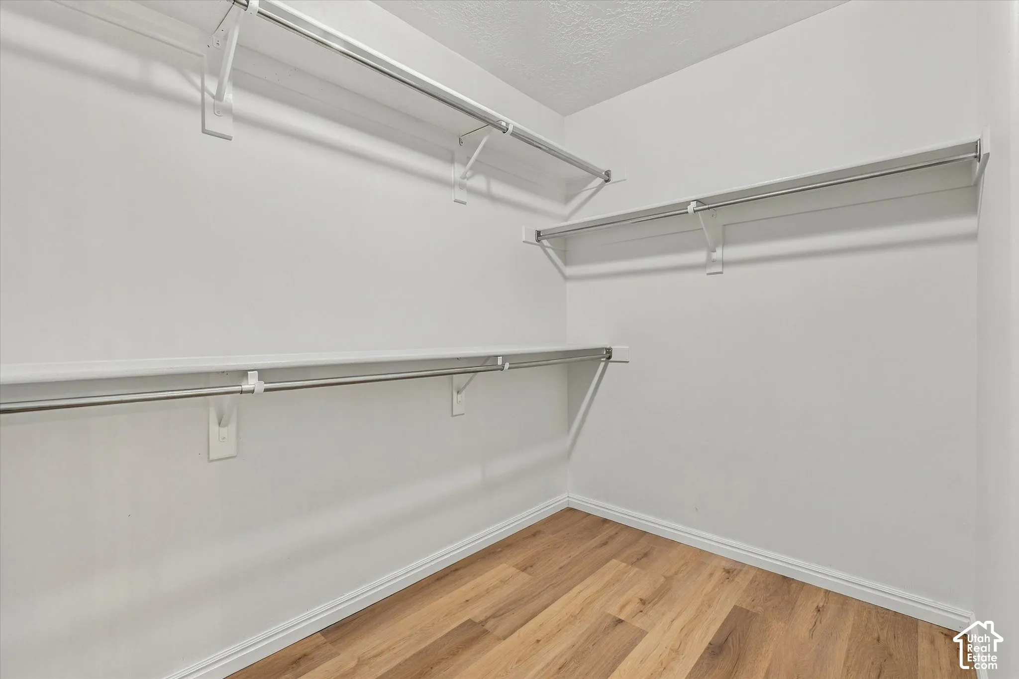 Walk-in closet featuring white walls, multi-level shelving, integrated hanging rods, and wood-finish flooring