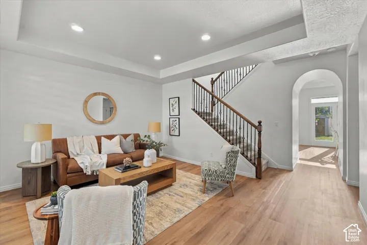 Recessed lighting, tray ceiling, wood-finish flooring, wrought iron stair balusters, and an arched entryway