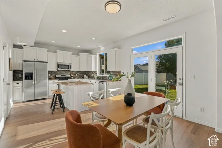 Kitchen featuring wood-finish flooring, white cabinetry, a central island with a beadboard base, stainless steel appliances, and a glass-paned door leading to the exterior