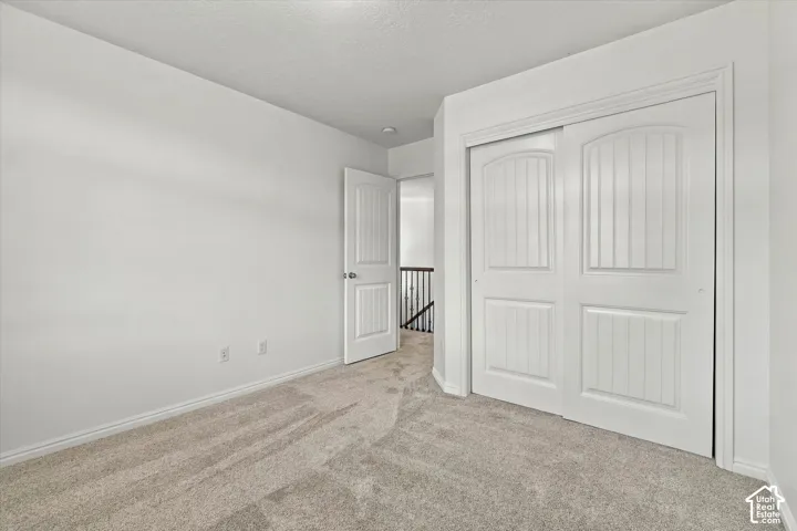 Neutral tone carpeting, white walls, white trim, and white sliding closet doors