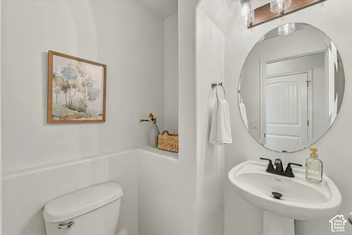 Pedestal sink with a matte black faucet, wall-mounted circular mirror, and overhead vanity lighting