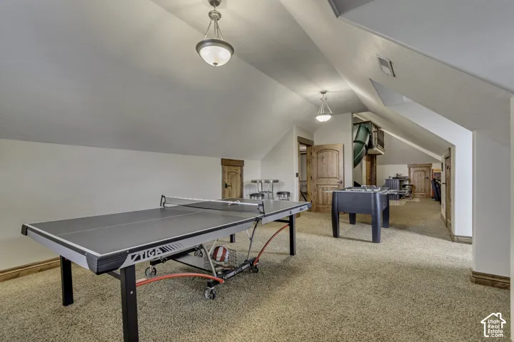 Carpeted recreation area featuring sloped ceilings, recessed lighting, and natural wood doors