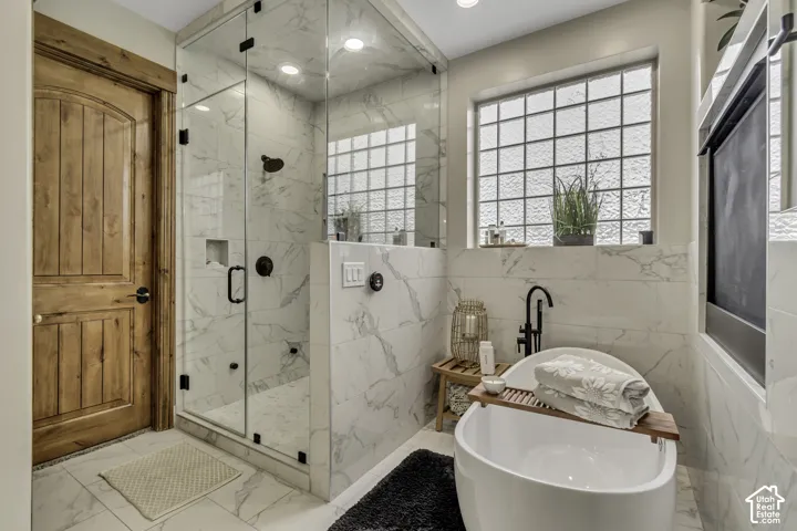 Freestanding soaking tub with a matte black faucet, glass-block window, and glass-enclosed shower with tile surround
