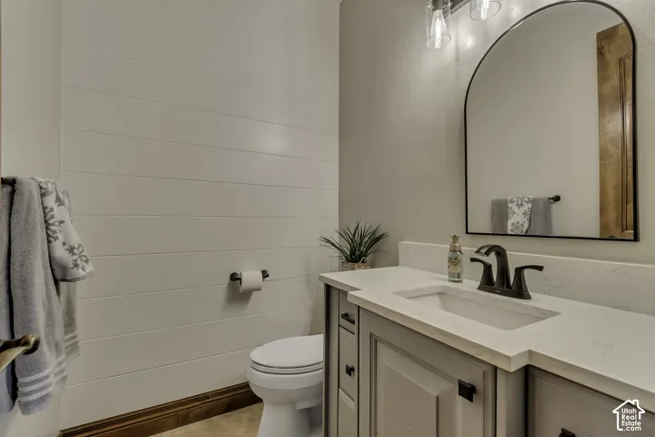 Shiplap accent wall, arched mirror, gray vanity with recessed panels, dark bronze hardware, and a white integrated sink with countertop