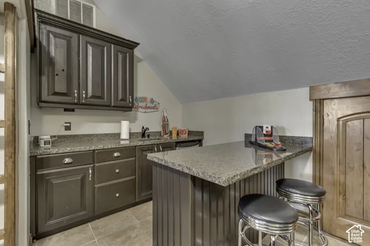 Built-in wet bar featuring dark cabinetry, stone countertops, an undermount sink, and tile flooring