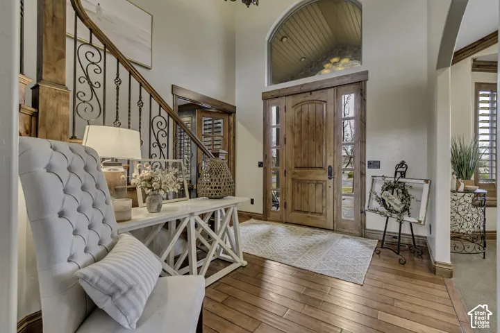 Wood-finish flooring, wood front door with sidelights, decorative iron stair railing, arched transom window, and architectural archway