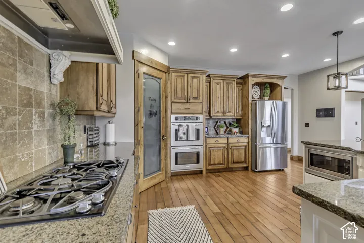 Kitchen featuring wood-finish flooring, granite countertops, a gas cooktop, built-in double ovens, and a paneled refrigerator