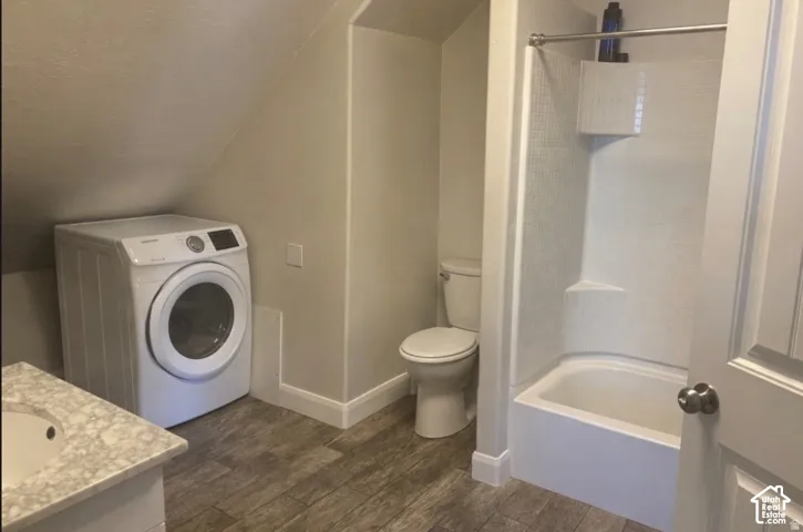 ADU White front-load washing machine, wood-finish flooring, white bathtub with shower, white toilet, and vanity with integrated sink