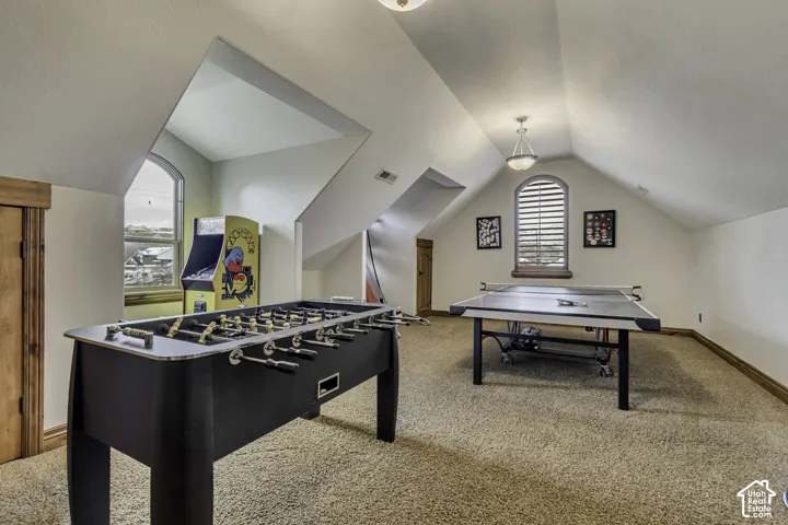 Spacious bonus room featuring vaulted ceilings, arched windows, built-in shelving, and neutral carpeting