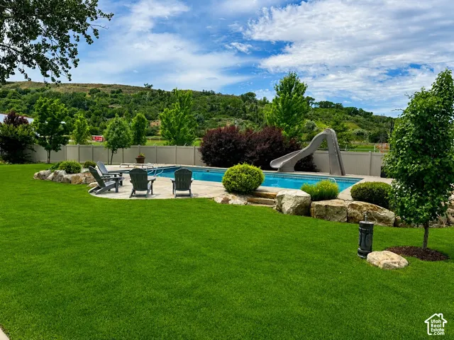 Expansive manicured lawn with a inground swimming pool, integrated waterslide, and a surrounding patio