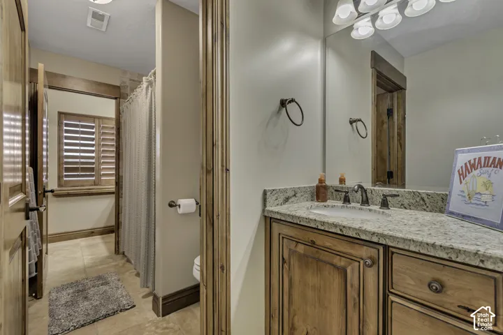 Bathroom featuring a wood-finish vanity with a stone countertop, an undermount sink, and a multi-light fixture