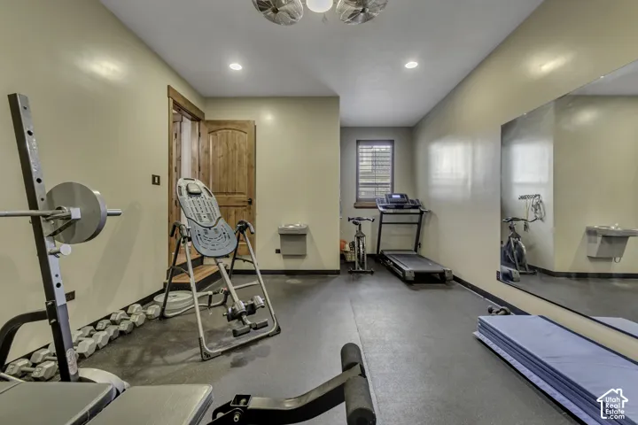 Dedicated exercise room featuring a rubberized floor, full-wall mirror, window with blinds, and recessed lighting