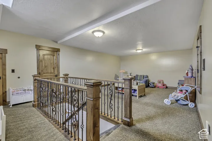 Spacious upper-level area featuring textured carpet flooring, wood-framed door, and an ornate wrought iron and wood banister