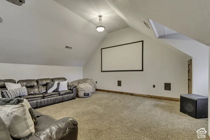 Carpeted attic space featuring a mounted projection screen, recessed wall panels, a wood-finish trim, and sloped ceilings with a central pendant light