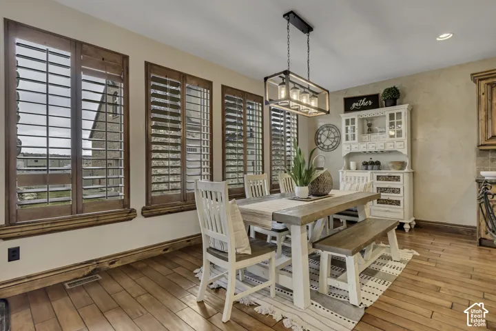 Wood-finish flooring, multiple windows with wood shutters, and a rectangular chandelier with exposed bulbs