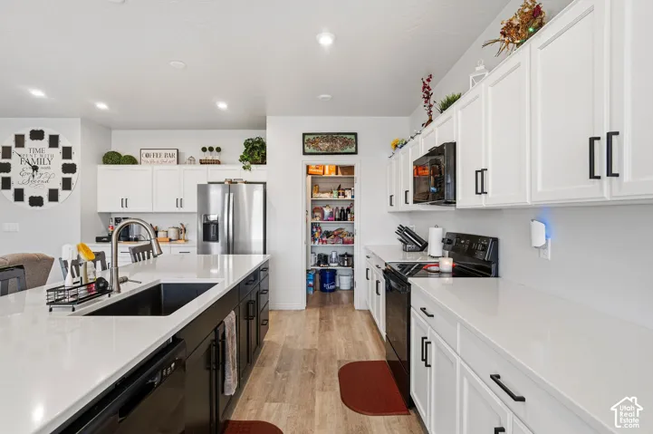 White cabinetry with black hardware, white countertops, wood-finish flooring, recessed lighting, and a walk-in pantry