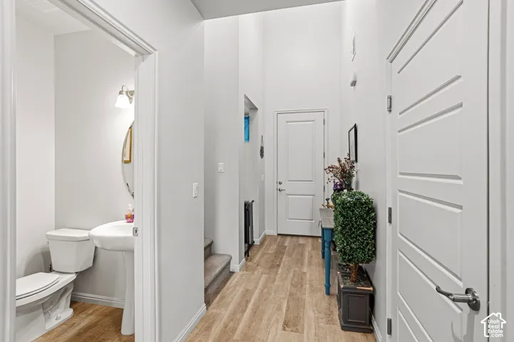 Hardwood-finish flooring extending through the entry, white interior doors with horizontal paneling, and a powder room featuring a pedestal sink and wall-mounted light fixture