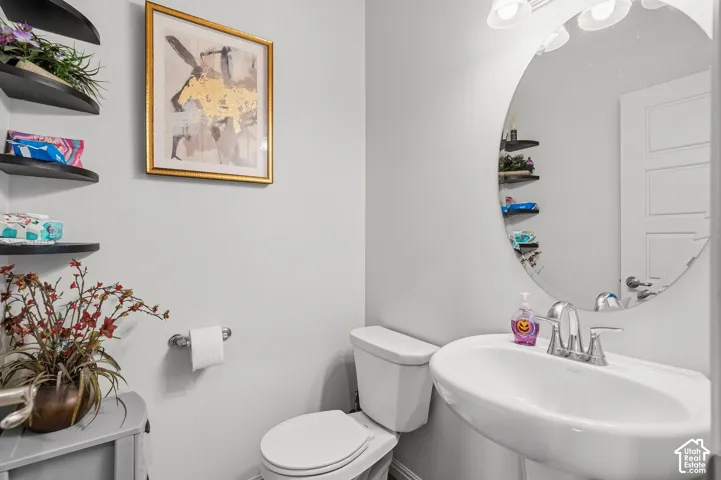 Pedestal sink with chrome faucet, circular mirror, and wall-mounted shelving
