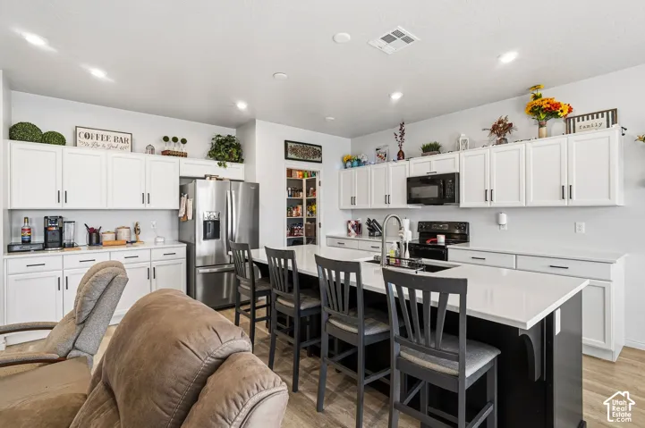 Well-appointed kitchen featuring white cabinetry, a large kitchen island with counter seating, stainless steel refrigerator, black range, and wood-finish flooring