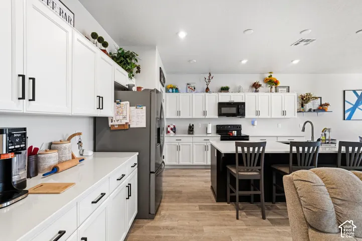 Kitchen featuring white cabinetry with black hardware, light-toned countertops, a central island with seating, dark wood-finish flooring, and recessed lighting