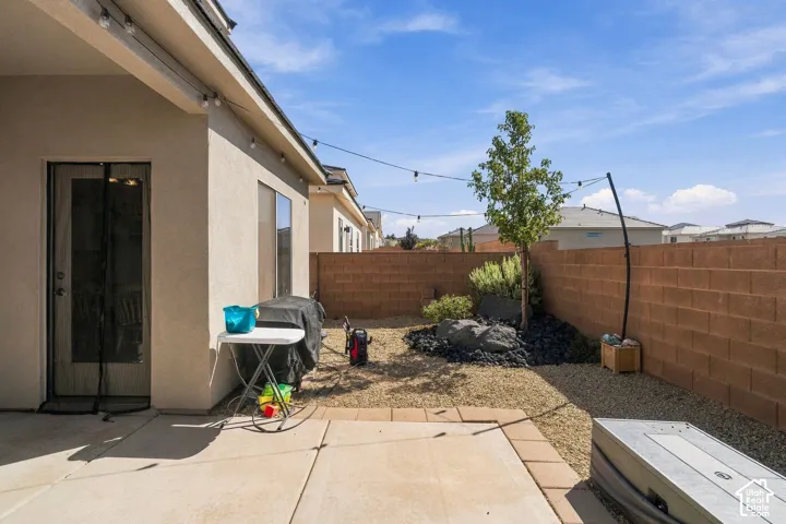 Paved patio with string lighting, stucco exterior, privacy wall, mature tree, and decorative rock landscaping