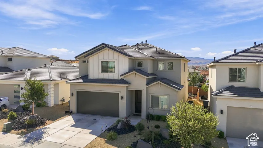 Contemporary two-story residence with a stucco and board and batten facade, featuring a two-car garage, concrete driveway, and xeriscaped front yard