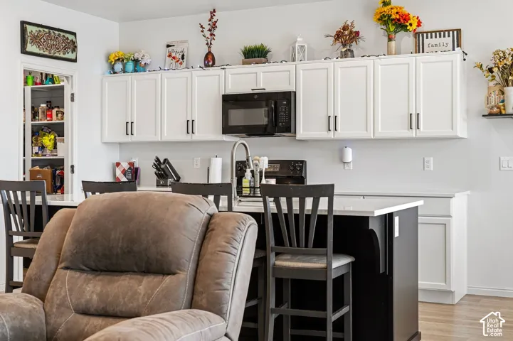 White cabinetry with dark hardware, black kitchen island, stainless steel sink with gooseneck faucet, black microwave, and pantry with shelving
