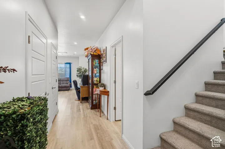 Light wood-finish flooring extending through the hallway, white walls, and recessed lighting
