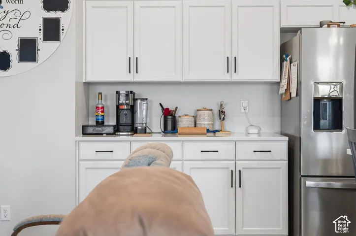 White shaker-style cabinetry with black hardware, light-colored countertops, and a stainless steel refrigerator