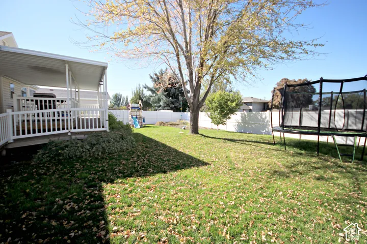 Expansive backyard featuring a covered patio, white deck railing, and a mature tree