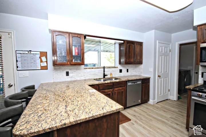 U-shaped granite countertop, wood cabinetry, stainless steel dishwasher, undermount sink with black faucet, and light wood-finish flooring