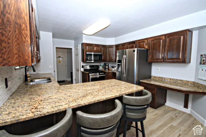 Kitchen featuring wood cabinetry, light-toned stone countertops, stainless steel appliances, and wood-finish flooring