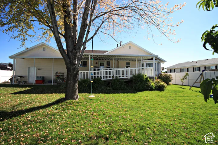 Expansive backyard with a covered patio, elevated wood deck with white railings, and a ramp for accessibility
