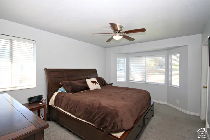 Expansive room featuring a bay window, ceiling fan, and carpeted flooring