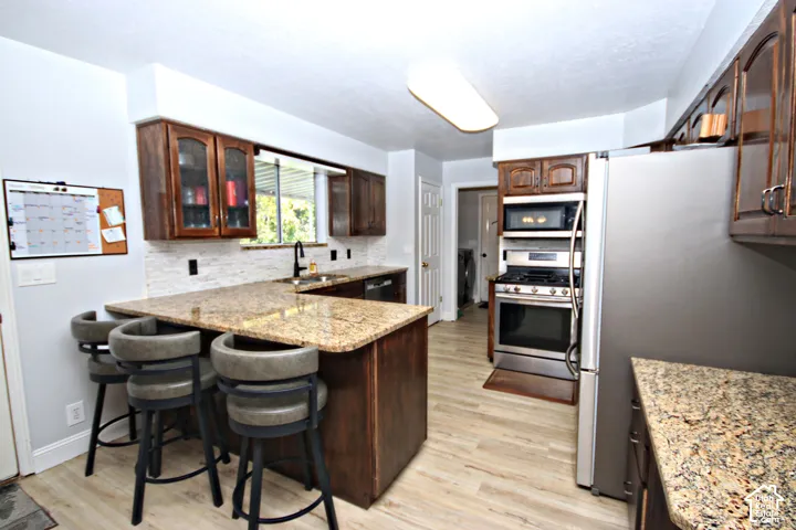 Kitchen featuring granite countertops, wood-finish cabinetry, stainless steel appliances, a tile backsplash, and wood-finish flooring