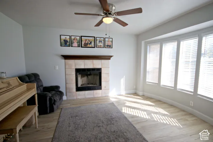 Tiled fireplace with a wood mantle and hearth, wood-finish flooring, and a ceiling fan with integrated lighting